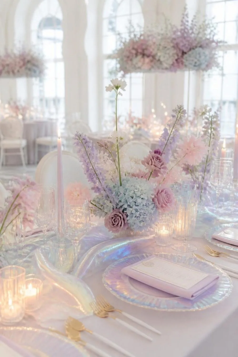 Iridescent pastel wedding centerpiece of lilac, blush and powder-blue flowers in a bright hall with tall arched windows