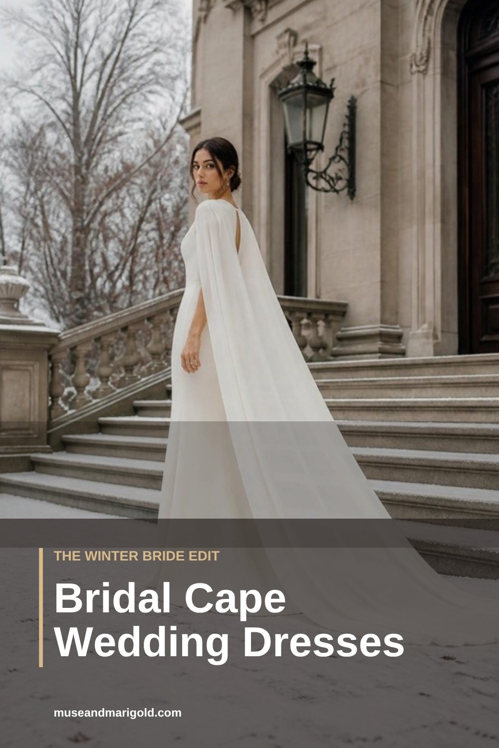 Bride in a fitted white gown and long sheer chiffon cape on a stone staircase outside a classic building with snowy trees