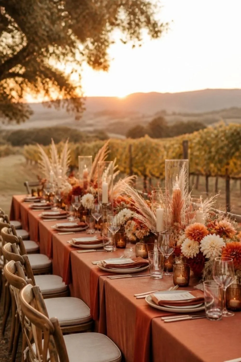 Long outdoor wedding reception table with terracotta linens, dried pampas and orange flowers above vineyard hi