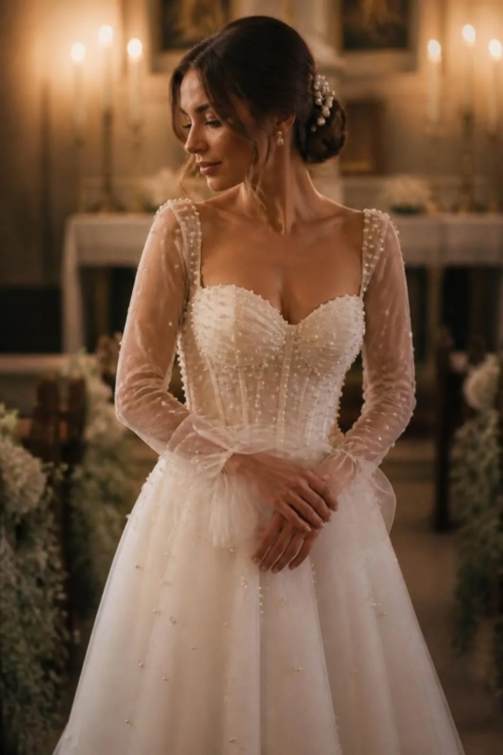 Bride in a sweetheart tulle wedding gown with sheer long sleeves scattered with pearls in a candlelit room wit